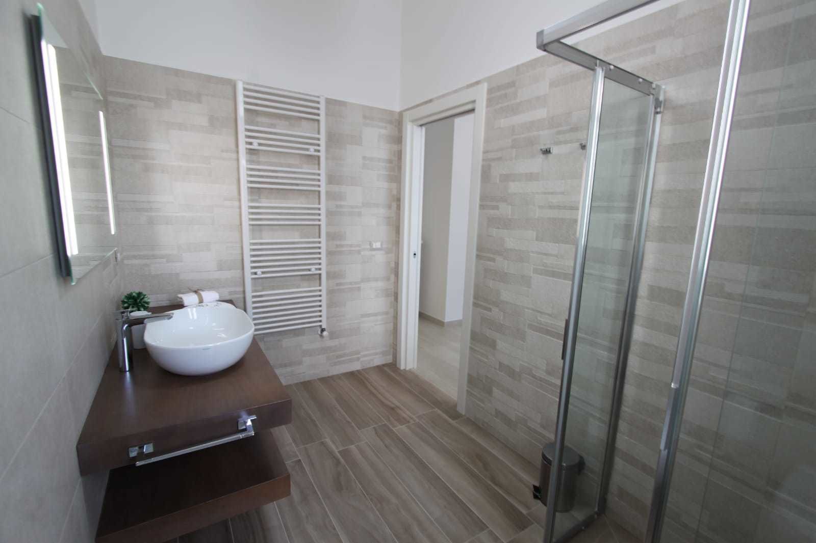 A modern bathroom with a large white sink, a glass shower enclosure, and a towel rack.
