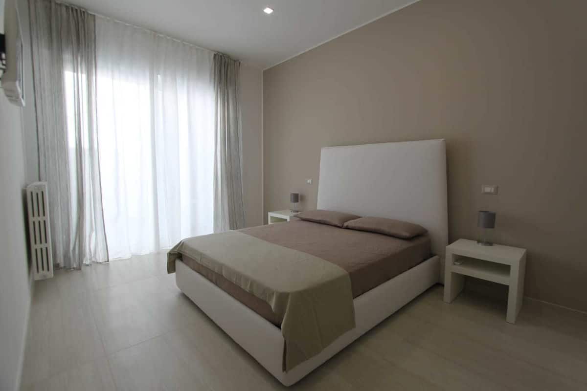 A modern bedroom with a large bed, white nightstands, and a radiator.