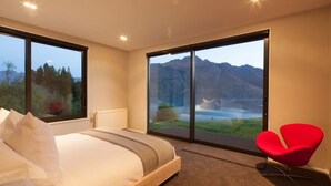 A bedroom with a large bed, a red chair, and a view of mountains through a sliding door.