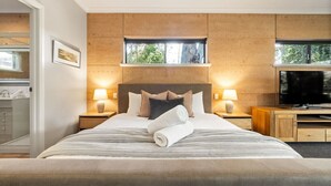 Une chambre d’hôtel moderne avec un grand lit, deux tables de chevet avec des lampes, une télévision et une vue sur la verdure par la fenêtre.