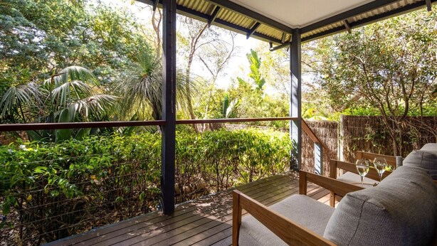 Une terrasse en bois dotée d’un espace salon confortable, entourée d’une végétation luxuriante et surmontée d’une structure à toit de chaume.
