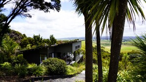 Una casa moderna con terraza, rodeada de exuberante vegetación y vistas a colinas distantes.