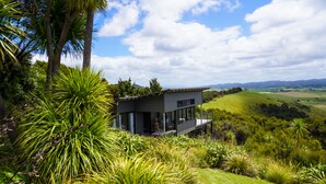 Una casa moderna con fachada de vidrio, rodeada de vegetación exuberante y un paisaje montañoso.