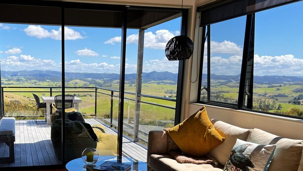 Un moderno salón con un gran ventanal que da a un balcón, con vistas panorámicas a campos verdes y montañas.