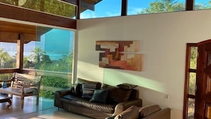 Un salon spacieux avec un grand canapé, une table basse et un lustre. Une grande fenêtre offre une vue sur l’extérieur.
