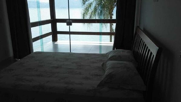 A bedroom with a bed, a view of the sea through large windows, and a balcony with a railing. - Biscaia- Beautiful house facing the sea in a gated community with a beach. (Angra dos Reis)