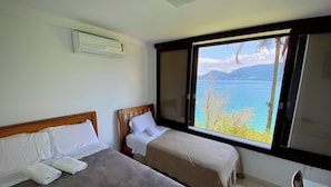 Une chambre avec deux lits, une fenêtre donnant sur la mer et un climatiseur fixé au mur.
