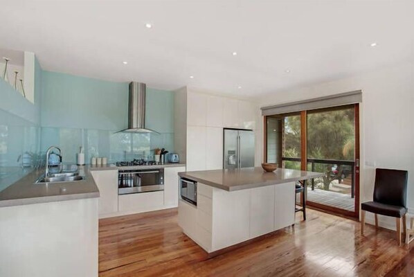A modern kitchen with a central island, stainless steel appliances, and a large window offering a view of the outdoors. - Convenient For Families, Golfers and Hot Spring Enthusiasts (Fingal)