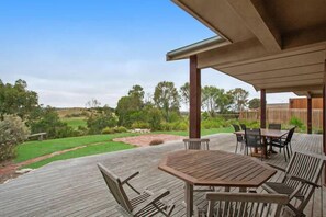 Un patio al aire libre con una mesa y sillas de madera, rodeado por una terraza de madera y un área cubierta.