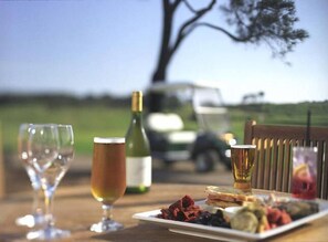 A picnic setup with a bottle of wine, glasses, and a plate of food on a table with a view of a tree and a vehicle in the background. - Convenient For Families, Golfers and Hot Spring Enthusiasts (Fingal)