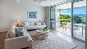 A modern living room with a sofa, coffee table, and a view of a balcony with outdoor furniture. - Lagoon 006 Hamilton Island by HamoRent (Hamilton Island)