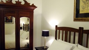 A hotel room with a bed, a nightstand with a lamp, and a wooden wardrobe with a mirror.