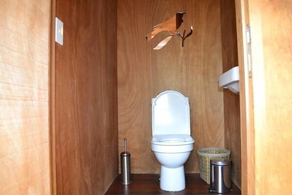 Een kleine houten badkamer met een wit toilet, een handdesinfecterend middel en een prullenbak.