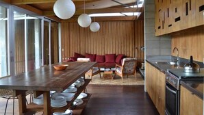 A modern kitchen with wooden cabinetry, a dining table with white plates, and a red sofa in the background.