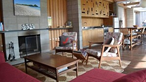 A modern living room with a fireplace, wooden furniture, and a view of the beach.