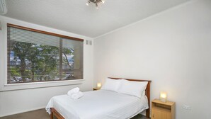 Ein Schlafzimmer mit einem Einzelbett, einem Nachttisch, einer Nachttischlampe und einem Fenster mit Jalousien.
