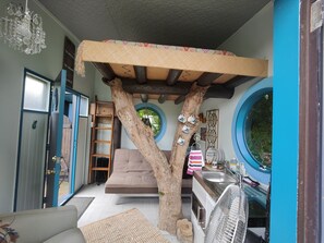 A cozy room with a tree structure, a sofa, a ladder, and a kitchen area with a sink and fan. - Big house for large families, responsible groups and your special celebration. (Waihi Beach)