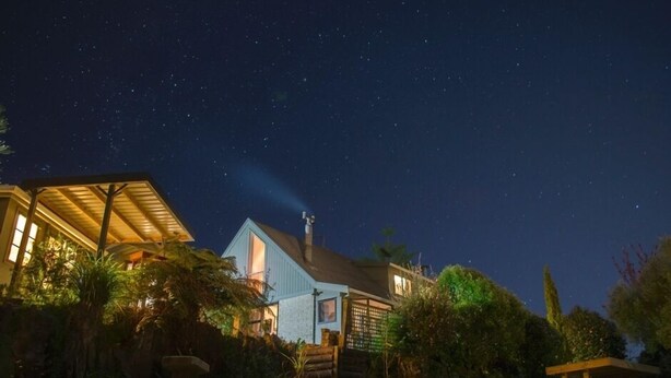 Ein Haus mit einer breiten Veranda und einem gut beleuchteten Innenraum bei Nacht.
