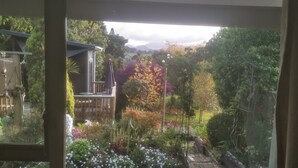 Blick von einem Balkon mit Holzboden auf einen Garten mit verschiedenen Pflanzen und einer Holzterrasse.