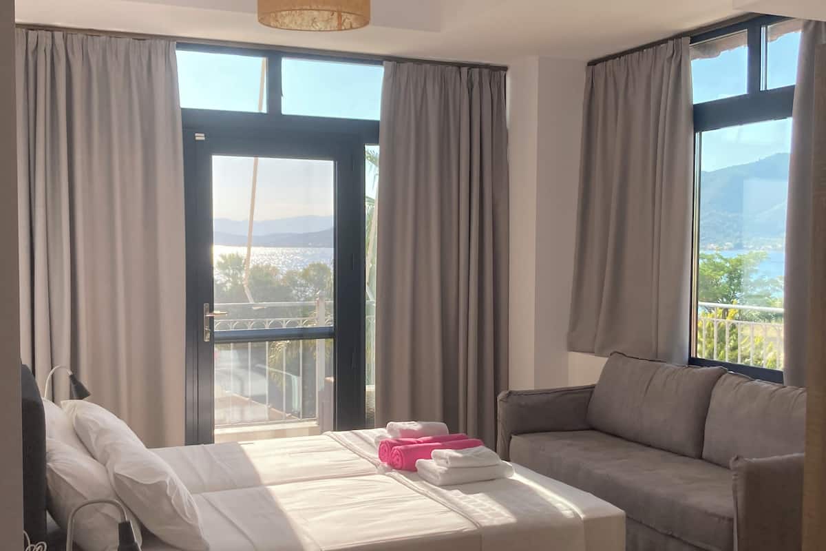 Ein Hotelzimmer mit einem Bett, einem Sofa und großen Fenstern mit Blick auf einen Balkon und Berge.