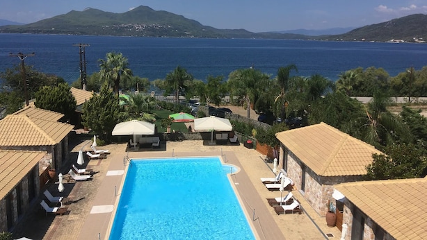 A pool area with lounge chairs and umbrellas, overlooking a body of water and hills. - Almyra Holiday Village (Istiaia-Aidipsos)