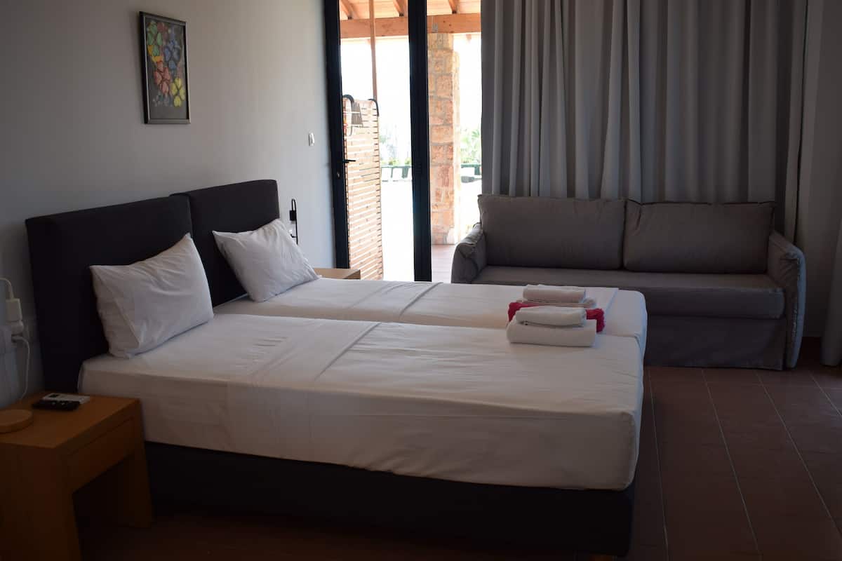 Ein Hotelzimmer mit zwei Betten, einer Couch, einem kleinen Tisch und einem Fenster mit Vorhängen.