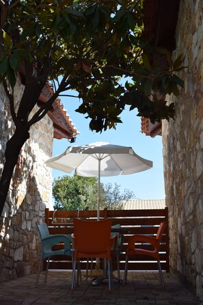 An outdoor patio with stone walls, a table with chairs, and an umbrella. - Almyra Holiday Village (Istiaia-Aidipsos)