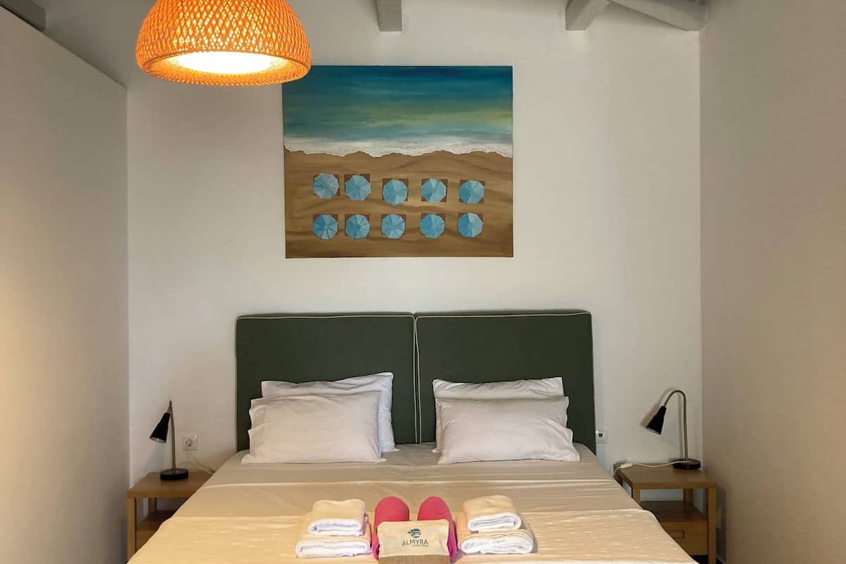 Ein Schlafzimmer mit einem Bett, zwei Nachttischen, einer Lampe, einem Strandbild und einer Pendelleuchte.