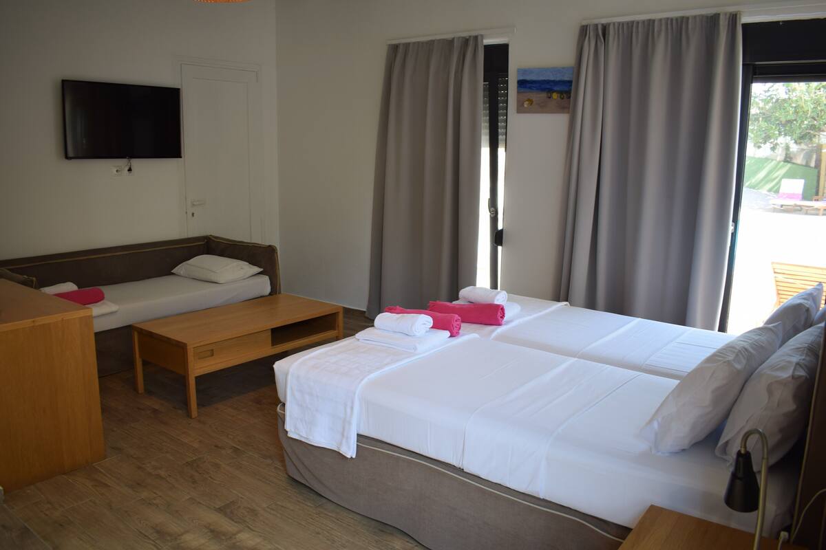 Ein Hotelzimmer mit zwei Betten, einem Fernseher, einem Holztisch und einem Fenster mit Vorhängen.