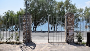 A gated entrance with stone pillars and metal fencing, leading to a beach area with trees and a view of the sea. - Almyra Holiday Village (Istiaia-Aidipsos)