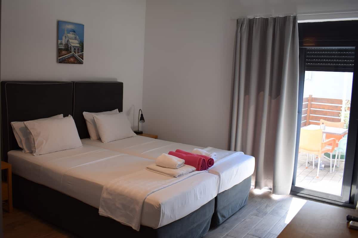 Ein Doppelbett mit weißen Leinentüchern und einem grauen Kopfteil, ein Gemälde eines Gebäudes an der Wand und ein Blick auf einen Außenbereich durch eine Schiebetür.