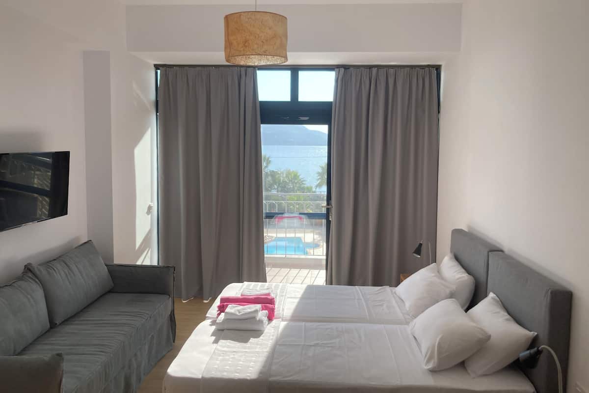 Ein modernes Hotelzimmer mit Bett, einer Couch, einem Fernseher und einem Balkon mit Blick auf einen Pool.