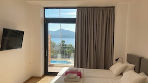 A hotel room with a bed, a TV, a balcony with a pool, and a view of a mountain. - Almyra Holiday Village (Istiaia-Aidipsos)