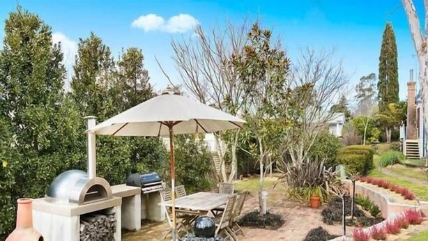 Uma área de pátio externa com churrasqueira, uma mesa e cadeiras, e um grande guarda-sol.