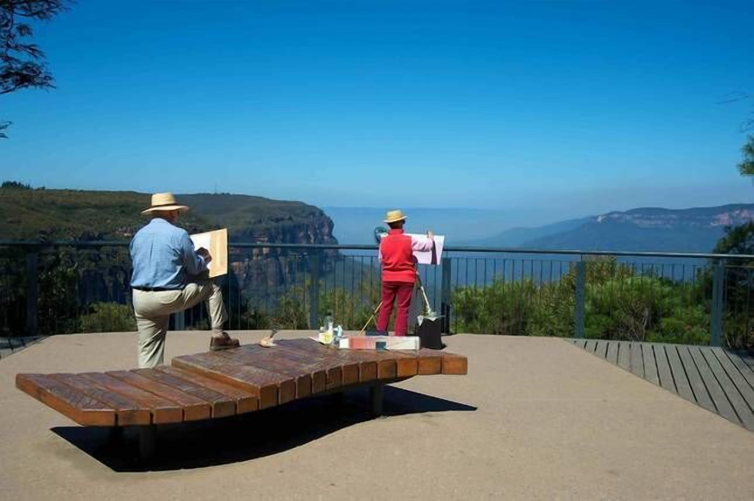Due persone dipingono una piattaforma di legno con una vista panoramica sullo sfondo.