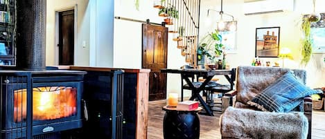 A cozy interior with a fireplace, wooden flooring, and a staircase with plants.