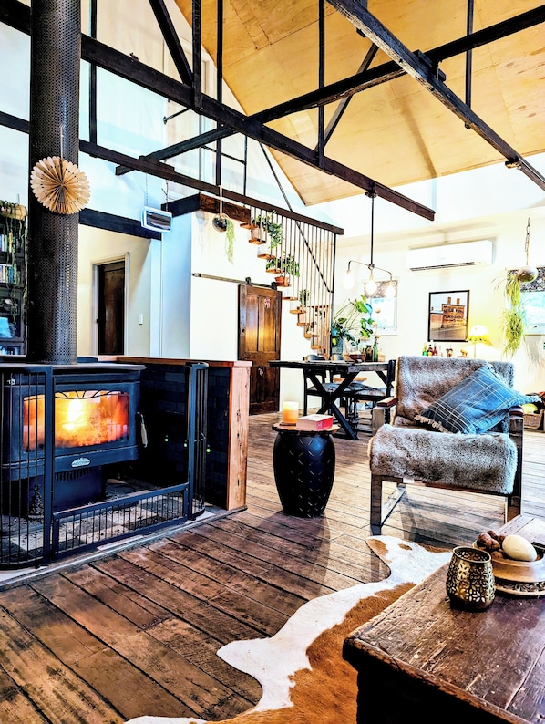Un interior acogedor con chimenea, piso de madera y una escalera decorada con plantas.