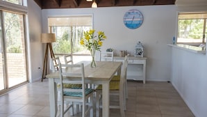A dining area with a wooden table and chairs, a vase with yellow flowers, a clock on the wall, and a lantern on a shelf. - Absolute Beachfront Penthouse | Panoramic Ocean Views | Batemans Bay Luxury (denhams beach)