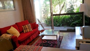 Ein Wohnzimmer mit einem roten Sofa, einem Glastisch und Blick auf einen Garten durch große Fenster.