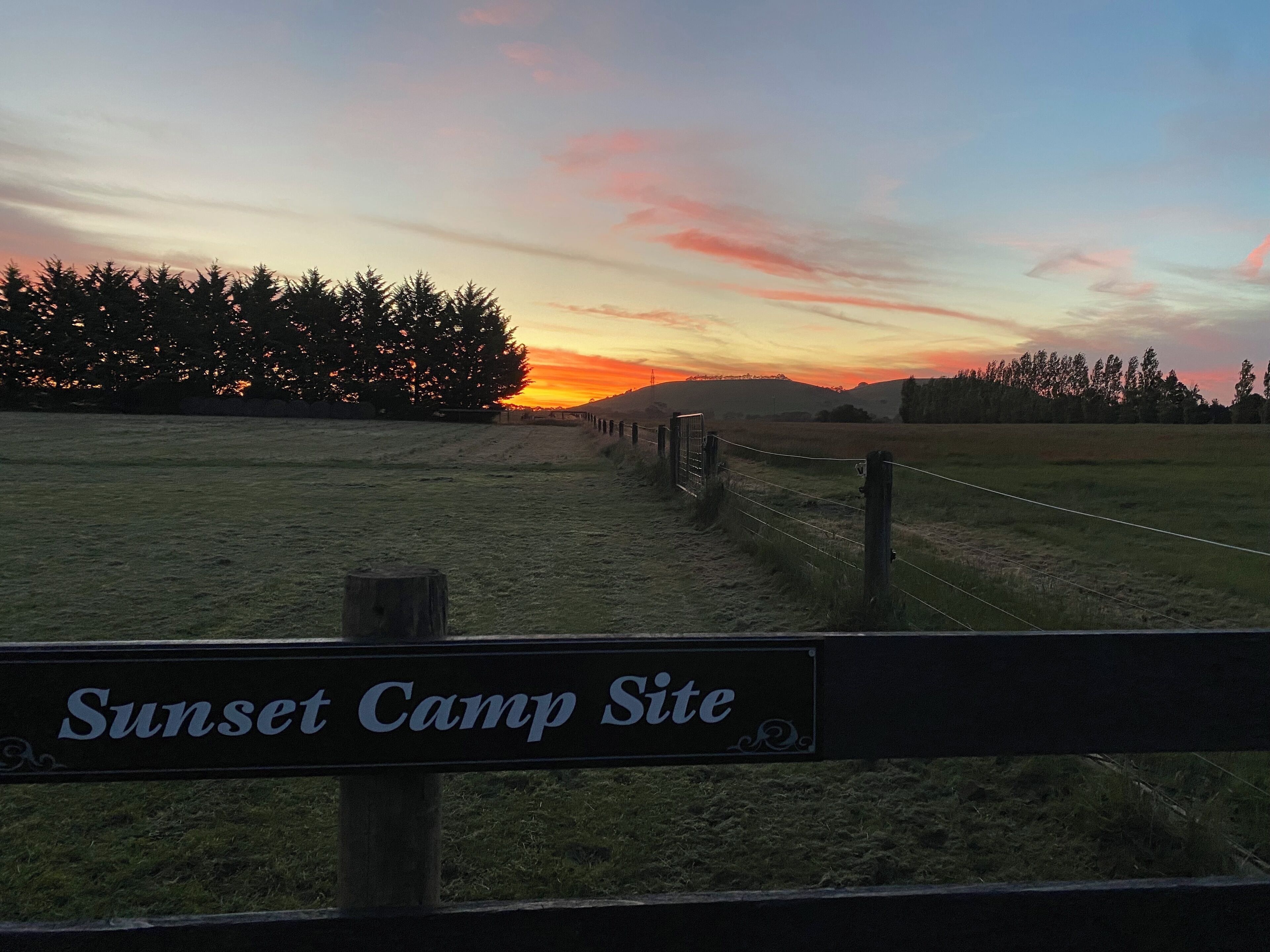 A sunset view at Sunset Camp Site with a wooden fence and a sign.