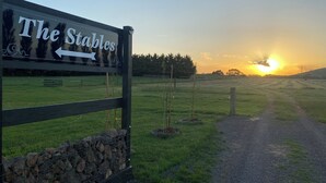 Señalización para 'The Stables' con una flecha indicadora, un sendero de grava y un atardecer de fondo.