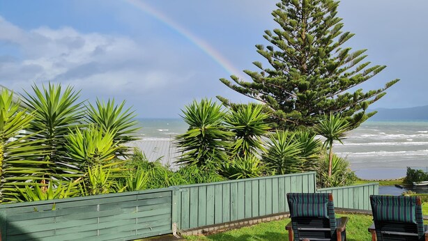 Uitzicht op een strand met een regenboog, palmbomen en een houten hek.