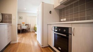 Una cocina con suelo de madera, armarios blancos y horno negro.