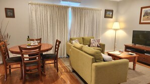 Una sala de estar con sofá, mesa de comedor con sillas, televisor y lámpara.
