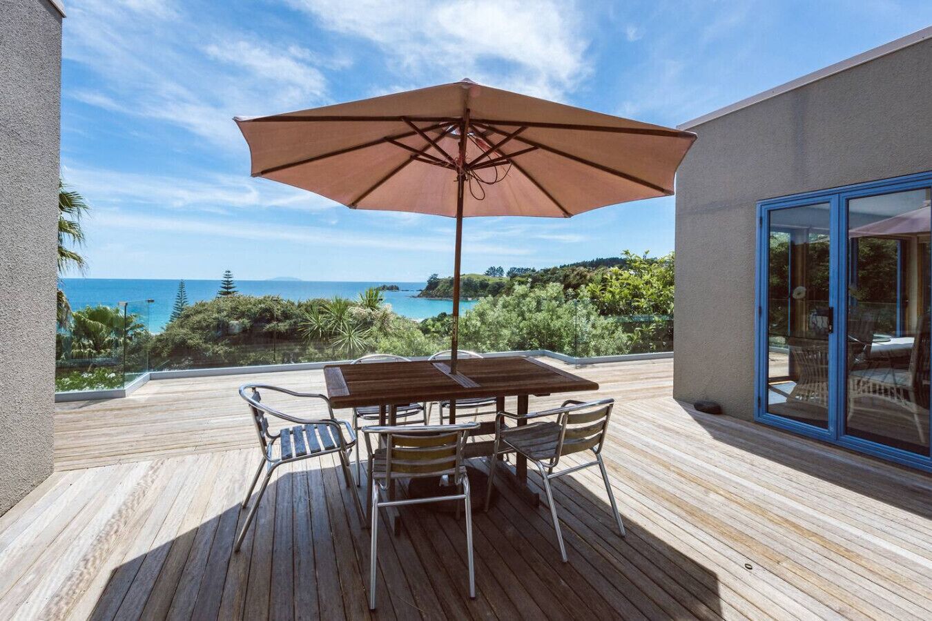 Eine Holzterrasse mit Tisch und Stühlen, einem Sonnenschirm und Blick aufs Meer.