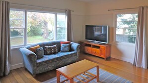 A living room with a sofa, TV, and a ceiling fan. - 6 Broome Street, Mallacoota (Mallacoota)