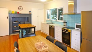 A modern kitchen with a wooden dining table, white cabinets, a built-in oven, and a stainless steel refrigerator. - 6 Broome Street, Mallacoota (Mallacoota)