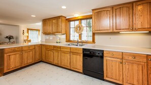 Une cuisine avec des meubles en bois, un lave-vaisselle et une fenêtre décorée d’une guirlande.