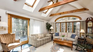 Un vaste salon doté d’un plafond haut, de poutres apparentes, de grandes fenêtres et d’un coin salon confortable avec un canapé et des fauteuils.