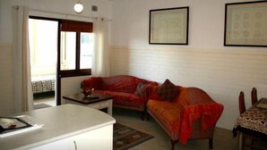 A living room with a sofa, a coffee table, and a dining table. There is a window with curtains, a framed picture on the wall, and a ceiling light. - B6 Walk to UWA close to SCGH & CBD (Crawley)